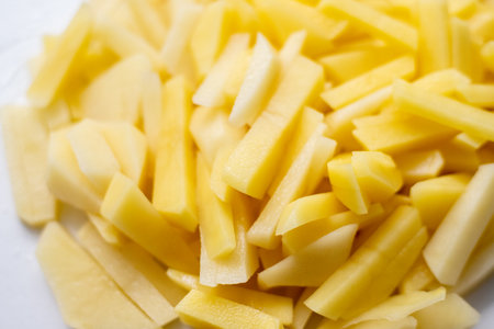 Raw potatoes cut into strips, close-up. Vegetable slices for cooking fried potatoes and French...