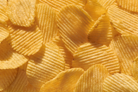 Food background of corrugated delicious golden crisp potato chips with texture close-up macro and sunlight, food pattern.の写真素材