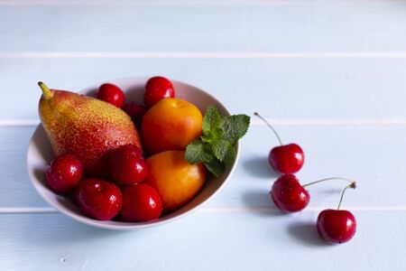 Fruit in a bowl. Red cherry, apricots, Forelle pear with fresh mint in a white bowl.の写真素材