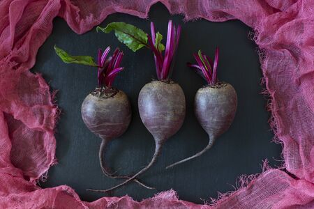Tree little fresh homegrown organic young beets with green leaves surrounded by purple fabric on dark wooden background.の写真素材