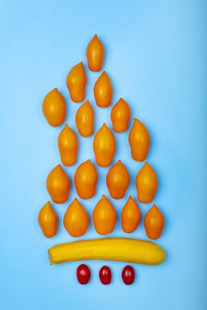Vegetable concept with orange tomatoes as a fire flame, yellow zucchini and cherry tomatoes on light blue background.の写真素材