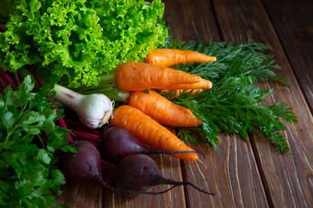 Fresh vegatable from farm market. Carrot and  beetroot with haulm, young garlic, parsley and lettuce on brown wooden background.の写真素材