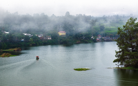 Beautiful scenery of huge lake, with trees, and mist create calming atmosphere. In the middle of the lake, there also a little boat  exploring the lakeの写真素材