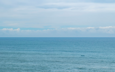 Small boat in almost empty sea, with beautiful cloudy sky, separated with sea by the horizon.の写真素材