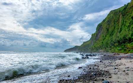 Photo of beautiful beach in cloudy day, when wave hit the beach. And with beautiful green cliff in the back. Captured on Menganti Beach, Kebumen, Indonesiaの写真素材