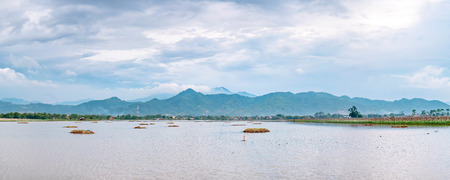 Panorama photo of very vast, broad, large, spacious pond, stretched into the horizon. Behind it is a line of hills and mountains that also expansive, and beautiful cloud yellow sky. This photo captured at afternoon, captured in Bandung, Indonesiaの写真素材