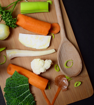 Vegetarian food ingredients and preparation. Soup ingredients on dark background with wooden kitchen utensils. Flat lay view.の写真素材