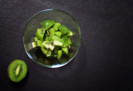 Detail of fresh green kiwi in glass bowl. Isolation over dark background. Dark moody food photography.の写真素材