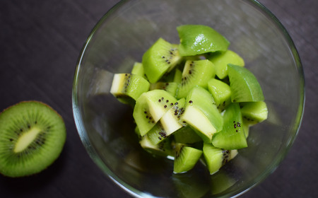 Detail of fresh green kiwi in glass bowl. Isolation over dark background. Dark moody food photography.の写真素材