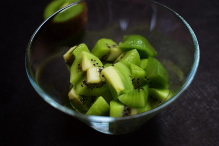 Detail of fresh green kiwi in glass bowl. Isolation over dark background. Dark moody food photography.の写真素材