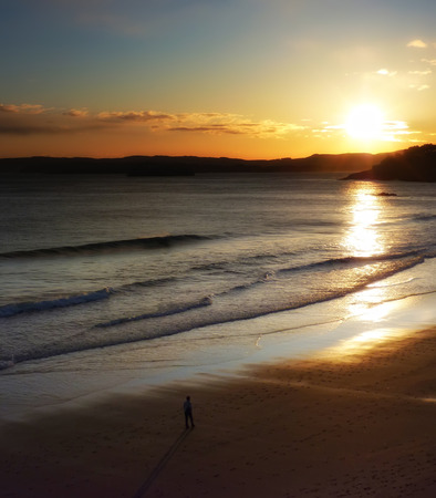 Silhouette of a person contemplating a new dawn from a beachの写真素材
