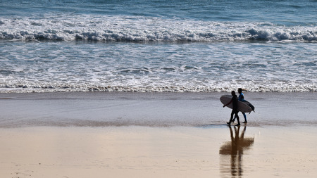 Pair of surfers walking on the beach ready to surfの写真素材