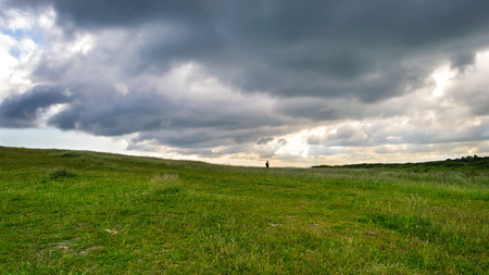 Lonely person walking in the meadow under the cloudsの写真素材