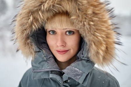 Beautiful girl with long curly hair and white clothes having fun outdoor in winter forest under snowflakes.の写真素材