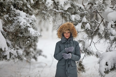 Beautiful girl with long curly hair and white clothes having fun outdoor in winter forest under snowflakes.の写真素材