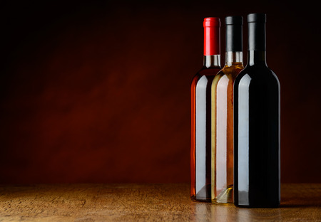 Red, white and rose wine in a row set on a wooden table.