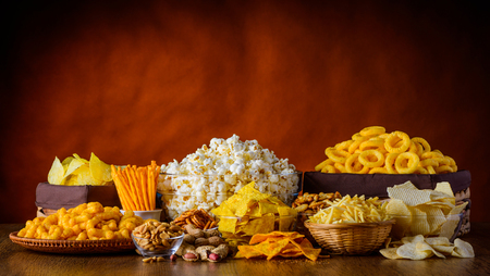 Different types of snacks, chips, nuts and popcorn in still life