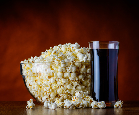 Bowl full with popcorn and a glass of cola on wooden tableの写真素材