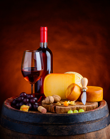 Rose wine in glass and bottle with grapes and gouda hard cheese and smoked cheese wheel on wooden barrelの写真素材