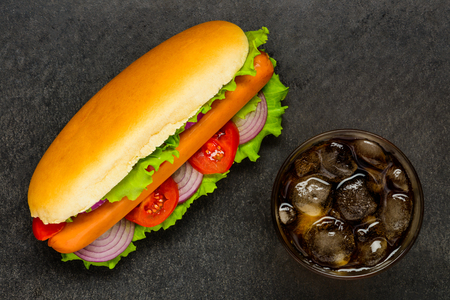 Hot Dog Sandwich with Sausage and Fresh Vegetables on a Dark Table with Glass Cold Colaの写真素材