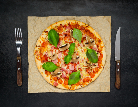 Fresh Baked Pizza with mushrooms, cheese and basil and Fork and Knife on a Dark Stone Table.の写真素材