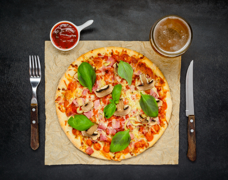Baked Pizza on a Dark Table with Tomato Sauce and a Glass of Golden Beerの写真素材