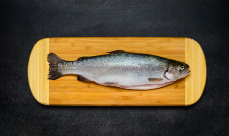 Raw Freshwater Trout Fish on Wooden Chopping board and on Dark Background