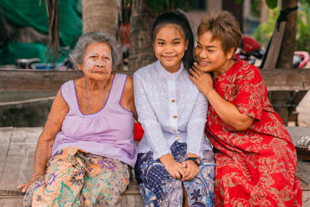 A beautiful Thai girl playing Khim, the traditional Thai music Instrument near the grandmother in outdoor on wooden panel. Leisure and hobby concept. Meditation by listening music.の写真素材