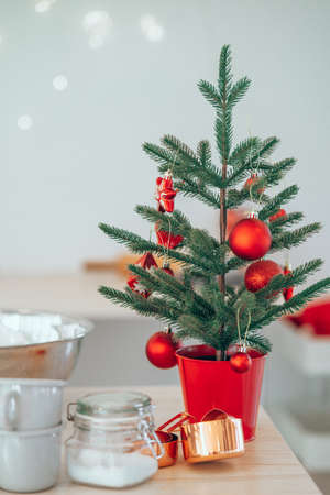 Decorated Christmas Tree in red pot placed on kitchen table near cups and sugar.の写真素材