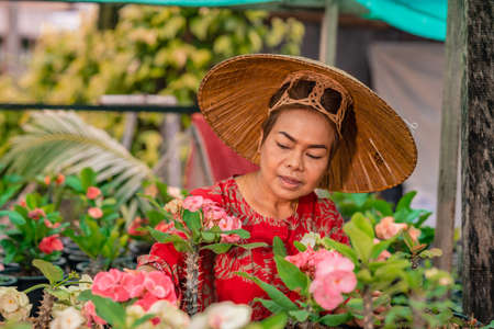 Happy asian woman with Vietnamese straw hat potting flowers in her garden