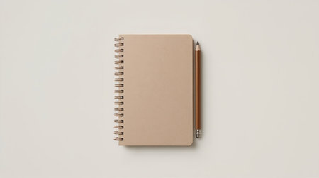 minimalist flat lay showing a small spiral notebook with a kraft cover placed beside a wooden pencil on a neutral background.の素材