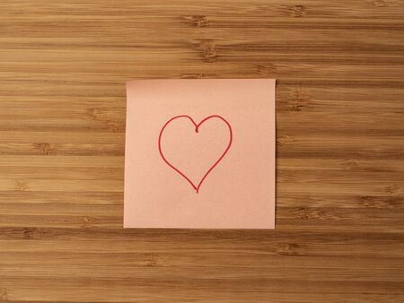 Sticker depicting the heart symbol. Paper sticker pasted on a wooden surface. Self-adhesive paper...