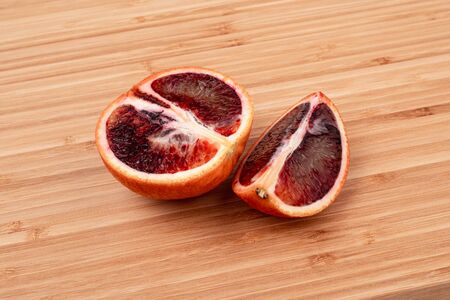 The blood orange is a variety of orange with crimson, almost blood-colored flesh. Image of a ripe orange on a wooden surface. Wood texture. Detailed photo. Soft shadows. Side view close-up.の写真素材
