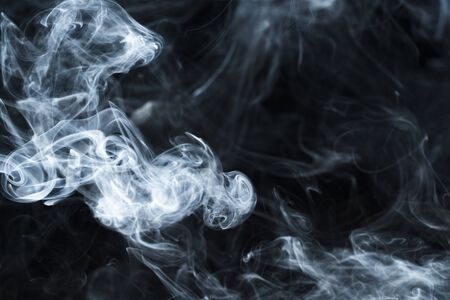 Background image of a wisp of smoke on a dark background. The texture of the flowing smoke. Frozen smoke on a dark background. Graphic resources dark backdrop. Texura of white clouds of fog. Curls of smoke frozen in motion.の写真素材