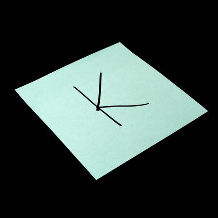Paper sticker with the image of the letter k. Isolated object on a black background. Paper texture. Sticky note. A piece of paper for notes. Self-adhesive piece of paper.の写真素材
