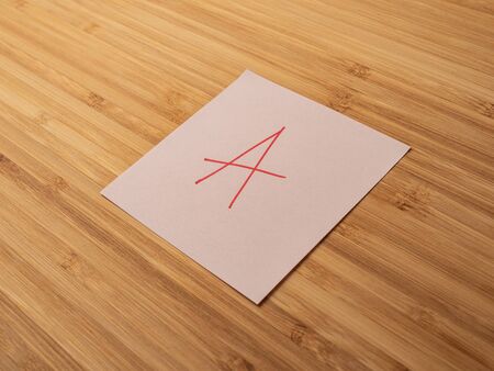 Sticker depicting the letter a. Paper sticker pasted on a wooden surface. Self-adhesive paper sheet. A piece of paper on a wooden board. Reminder for action. Paper sheet for notes.の写真素材
