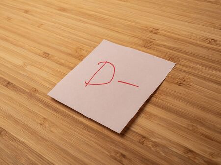 Sticker depicting the letter d. Paper sticker pasted on a wooden surface. Self-adhesive paper sheet. A piece of paper on a wooden board. Reminder for action. Paper sheet for notes.の写真素材