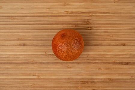 The blood orange is a variety of orange with crimson, almost blood-colored flesh. Image of a ripe orange on a wooden surface. Wood texture. Detailed photo. Soft shadows. Top view close-up.の写真素材