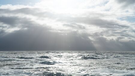 Graphic resources background image of a cloudy sky over a glacier. Ice covered sea in the winter season. Bright sunlight breaks through the clouds. Desert landscape of a frozen reservoir.の写真素材
