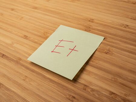 Sticker depicting the letter e. Paper sticker pasted on a wooden surface. Self-adhesive paper sheet. A piece of paper on a wooden board. Reminder for action. Paper sheet for notes.の写真素材