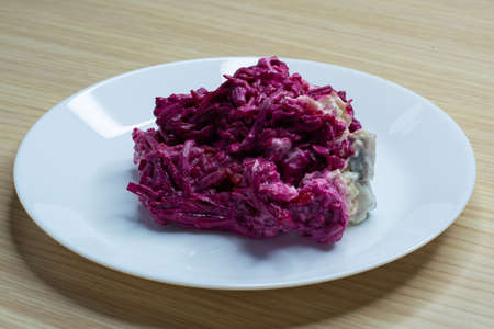 Herring salad under a fur coat on a white plate on a wooden tableの写真素材