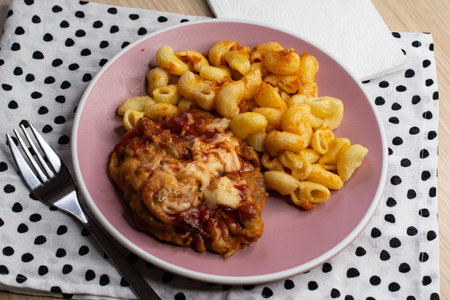 Chicken pasta with tomato sauce and cheese on a pink plate with napkinsの写真素材