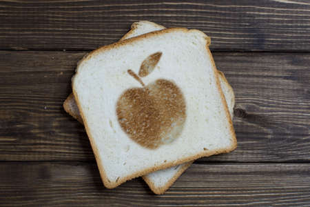 toast with the sign apple on dark wood. An apple with a leaf burnt on bread.の写真素材