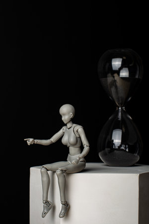 A woman sitting on a plaster prism indicates the direction. The hourglass is behind. Composition in the dark key.の写真素材