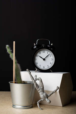 The clock stands on a plaster prism. The cactus grows from a metal bucket. The man stands on one hand. Composition in the dark key.の写真素材