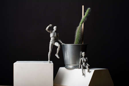 The man is trying to climb up to the cacus. A woman sits leaning on an iron pot.の写真素材