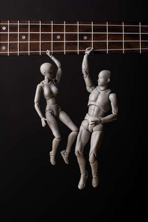 People hang on a ukulele string. The woman and the man hold tight to the string. On a dark background. Music in our hearts.の写真素材