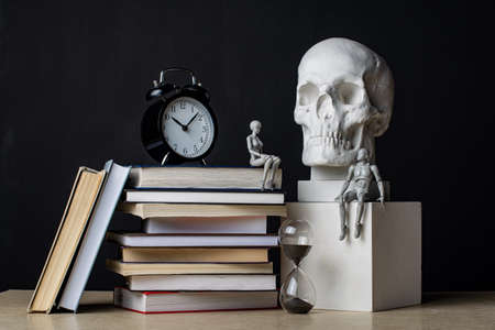 A man sits on a plaster cube near the skull. A woman sits on a stack of books near the clock. The couple exchanged glances. Composition in the dark key.の写真素材