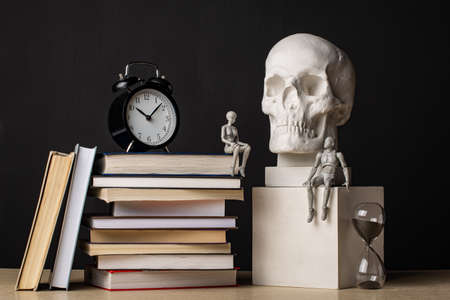 A man sits on a plaster cube near the skull. A woman sits on a stack of books near the clock. The couple exchanged glances. Composition in the dark key.の写真素材