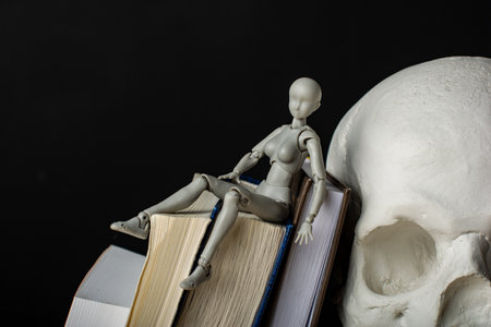 A woman lies on a pile of books, next to a plaster skull. Composition in the dark key.の写真素材